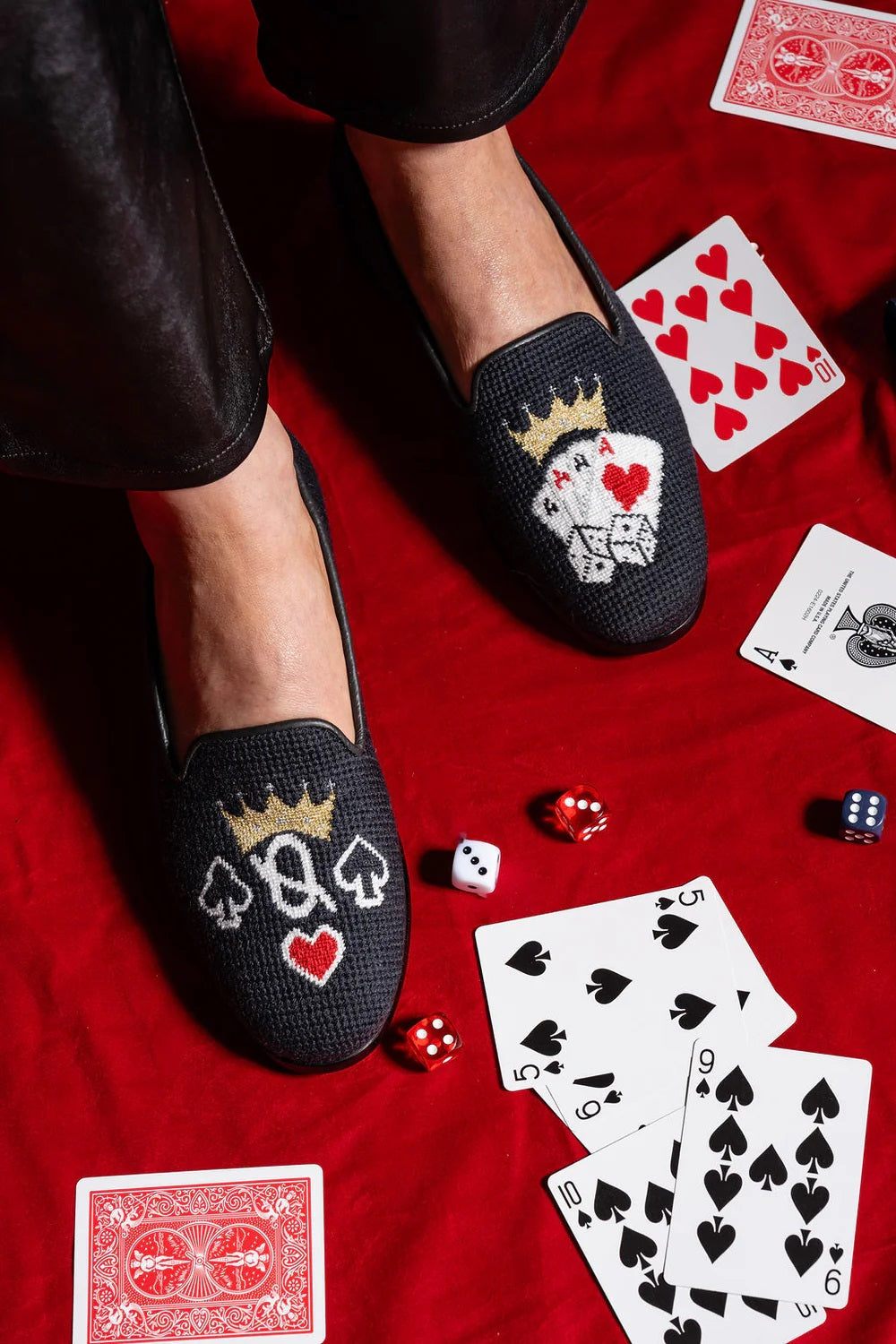 A pair of black needlepoint loafers with a queen and crown design, displayed alongside a red card and suggesting your favorite card games poker, bridge and more