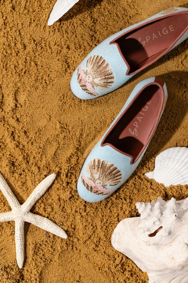 Pair of light blue loafers with shell design on a sandy background with shells and starfish.
