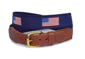 The American Flag in red white and blue sits on a a navy ribbon  background and finished with navy webbing, leather tabs and a brass buckle .