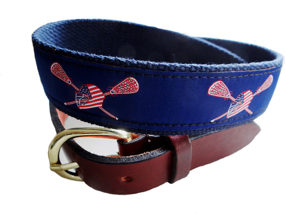Popular Boys preppy lacrosse belt with navy background is complimented with red white and blue Helmut and sticks. Leather Tabs and brass buckle complete the construction.
